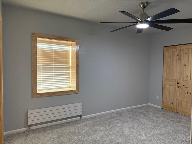 unfurnished bedroom with a closet, baseboards, light colored carpet, and radiator heating unit