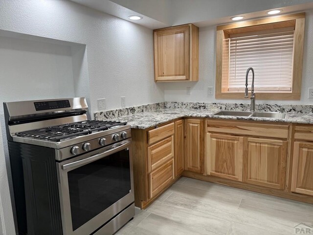 kitchen featuring stainless steel gas range, recessed lighting, a sink, and light stone countertops