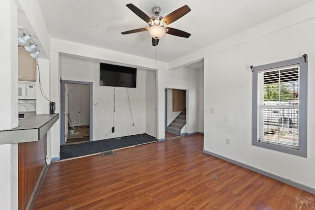 616 E 5th St, Pueblo, CO 81001 - unfurnished living room featuring visible vents, stairs, baseboards, ceiling fan, and dark wood-style floors
