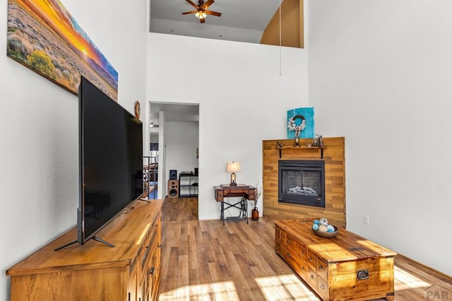 living area featuring a fireplace, wood finished floors, a towering ceiling, and a ceiling fan