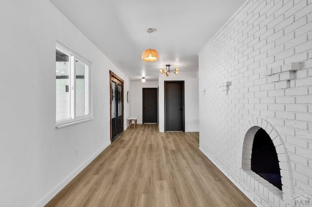 interior space with brick wall, light wood finished floors, a brick fireplace, and baseboards