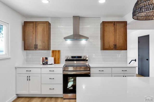 kitchen featuring brown cabinetry, white cabinets, electric stove, light countertops, and wall chimney range hood