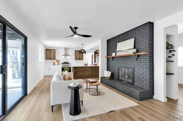 living area featuring light wood finished floors, a brick fireplace, a ceiling fan, and baseboards