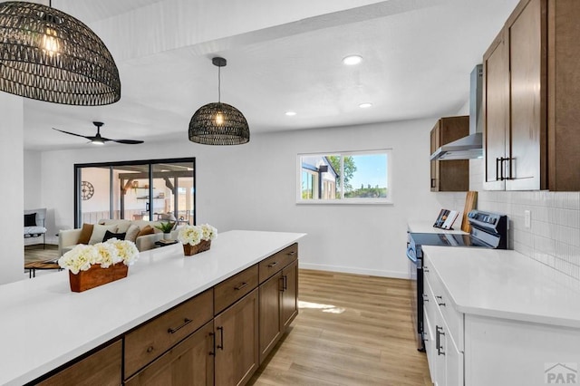 kitchen featuring light countertops, hanging light fixtures, electric range, light wood-type flooring, and wall chimney exhaust hood