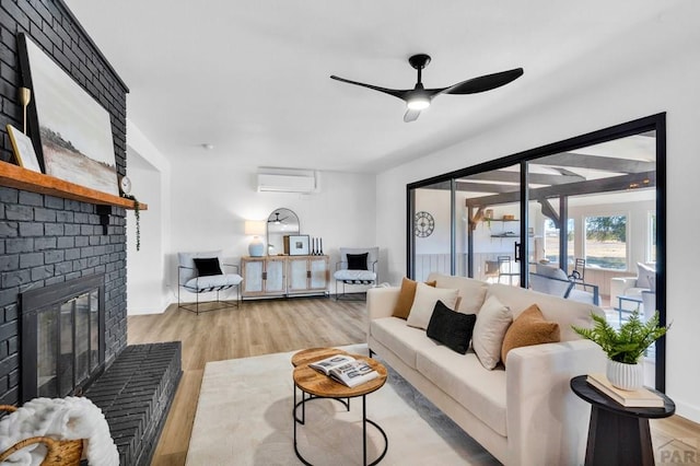 living room with light wood-type flooring, a wall mounted air conditioner, a ceiling fan, and a brick fireplace