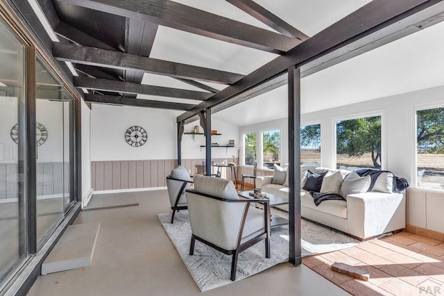 living room featuring vaulted ceiling with beams, concrete flooring, and wainscoting