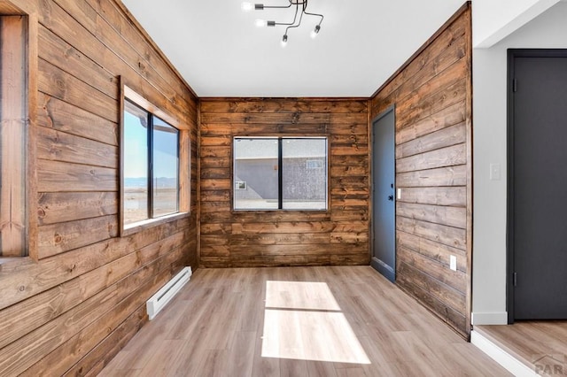 spare room featuring light wood-type flooring, a baseboard radiator, wooden walls, and baseboards