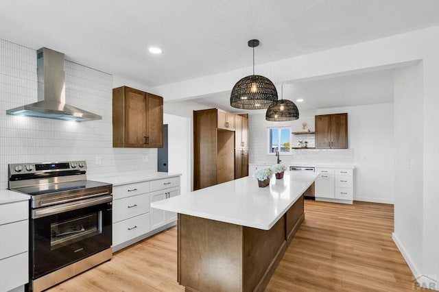 kitchen featuring stainless steel appliances, light countertops, white cabinetry, a kitchen island, and wall chimney exhaust hood