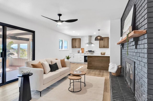 living area featuring light wood-style floors, a fireplace, a ceiling fan, and a healthy amount of sunlight