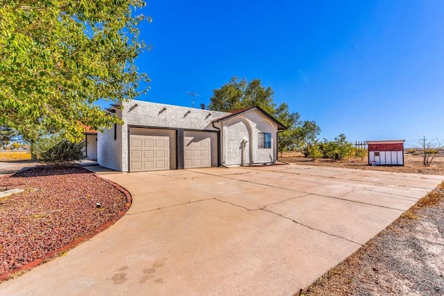 view of front of house featuring a garage, concrete driveway, a storage shed, and stucco siding