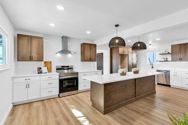 kitchen featuring white cabinets, light countertops, appliances with stainless steel finishes, wall chimney exhaust hood, and decorative light fixtures