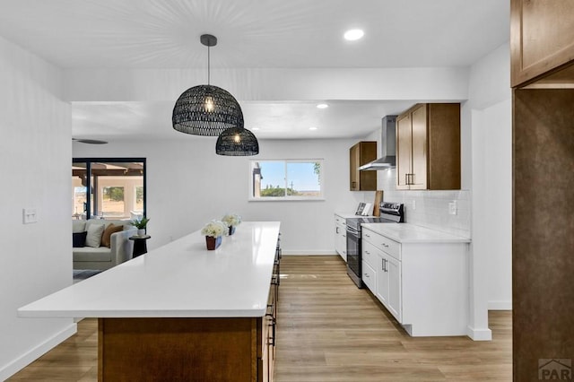 kitchen featuring decorative light fixtures, stainless steel electric stove, light countertops, decorative backsplash, and wall chimney range hood