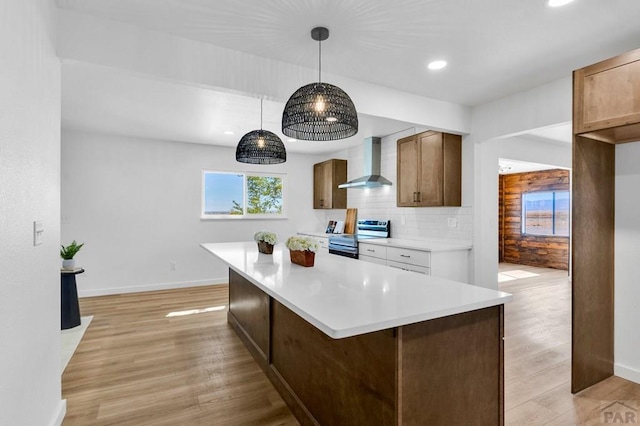 kitchen featuring brown cabinets, light countertops, hanging light fixtures, wall chimney range hood, and stainless steel electric range