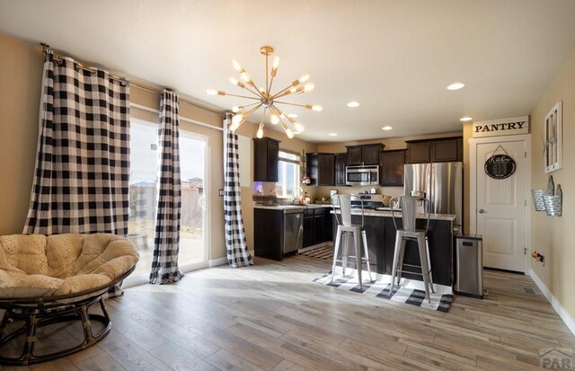 kitchen featuring a center island, light wood finished floors, stainless steel appliances, dark brown cabinetry, and a kitchen breakfast bar