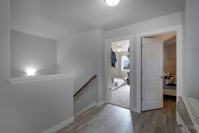 hall featuring baseboards, wood finished floors, and an upstairs landing