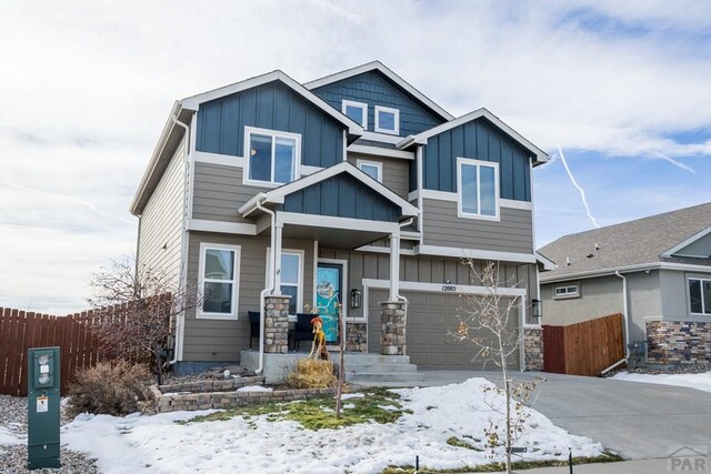 craftsman inspired home with a garage, fence, driveway, stone siding, and board and batten siding