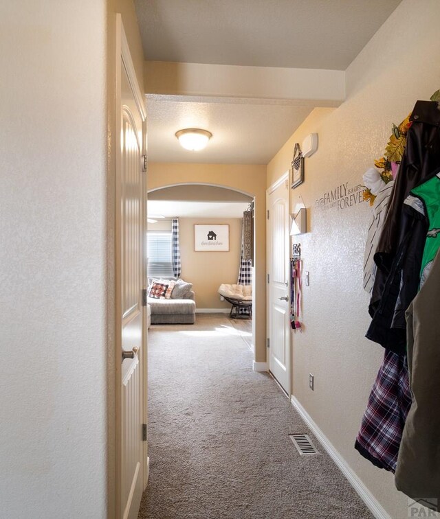 hall with carpet, arched walkways, visible vents, a textured wall, and baseboards