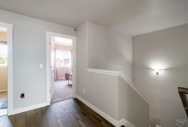 corridor featuring dark wood-type flooring, baseboards, a healthy amount of sunlight, and an upstairs landing