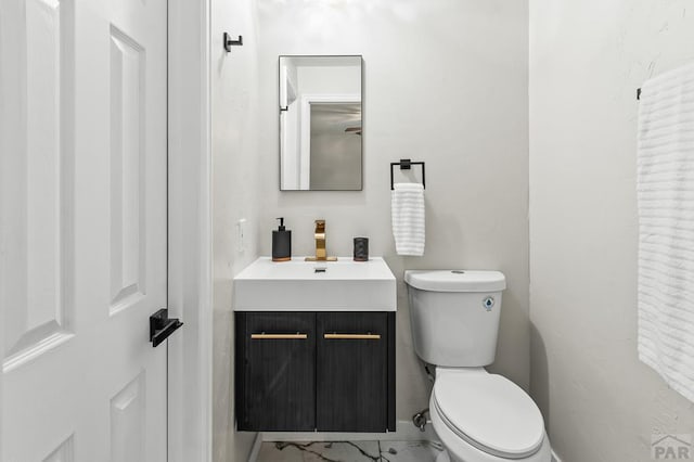 half bathroom with marble finish floor, vanity, and toilet