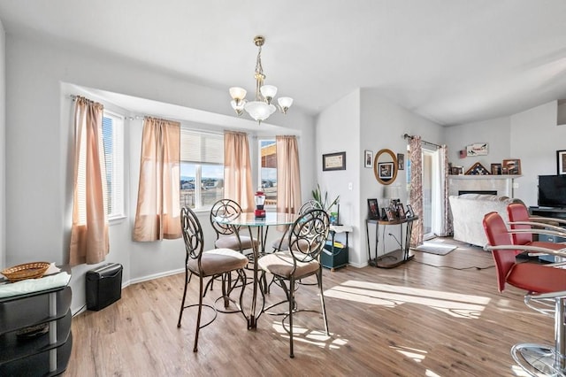 dining area with baseboards, an inviting chandelier, a fireplace, and light wood-style floors