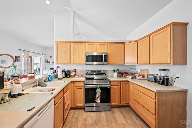 kitchen featuring lofted ceiling, stainless steel appliances, a sink, light wood-style floors, and light countertops