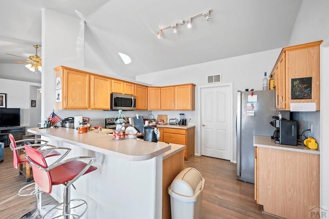 kitchen with a breakfast bar area, stainless steel appliances, light countertops, visible vents, and a peninsula