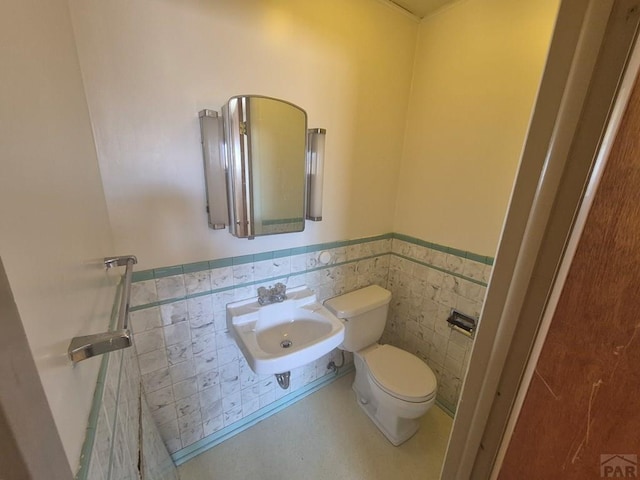 bathroom featuring tile walls, a wainscoted wall, a sink, and toilet