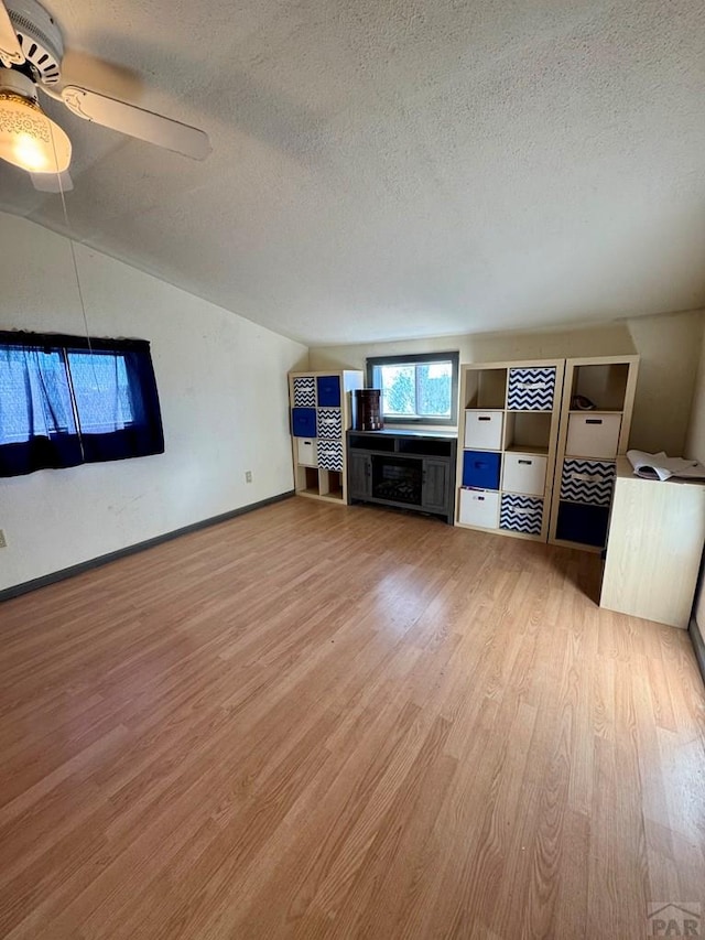 unfurnished living room with lofted ceiling, a ceiling fan, a textured ceiling, wood finished floors, and baseboards