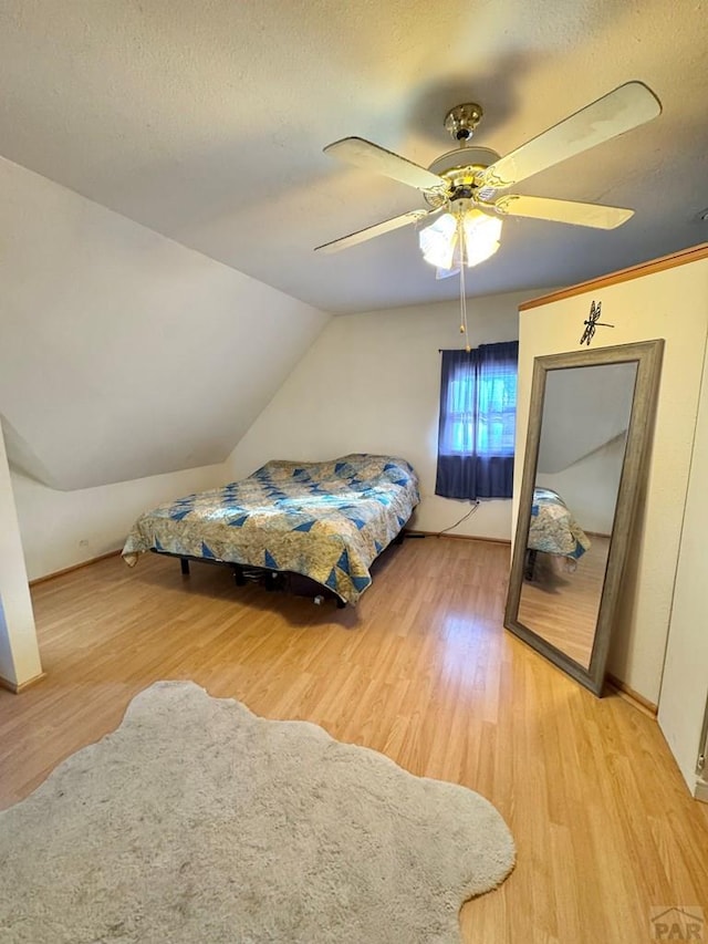 bedroom featuring vaulted ceiling, a textured ceiling, wood finished floors, and a ceiling fan