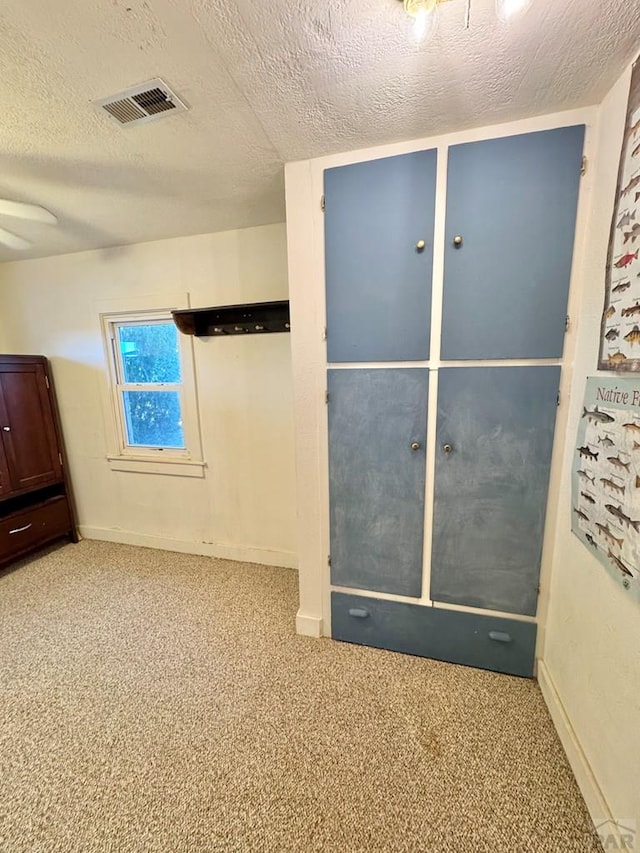 unfurnished room featuring a textured ceiling, carpet floors, visible vents, and baseboards