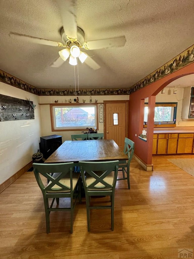 dining area with arched walkways, baseboards, light wood-style flooring, and a textured ceiling