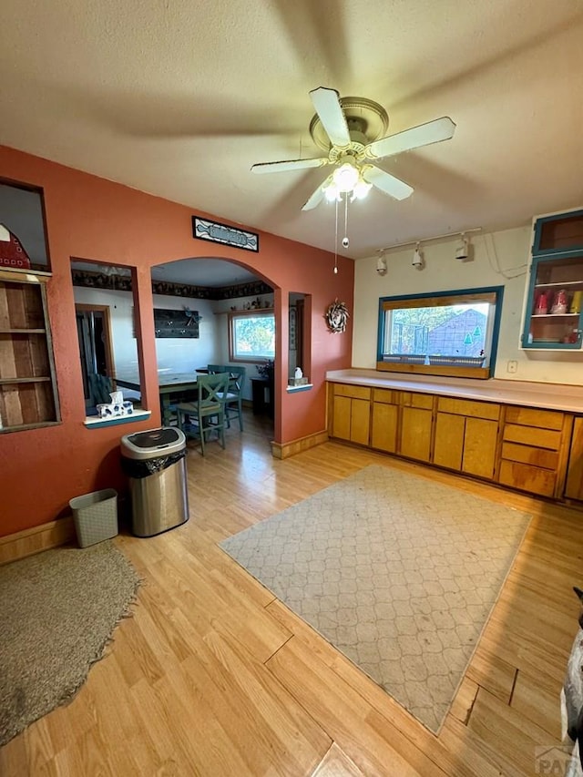 interior space with arched walkways, light wood-style floors, ceiling fan, a textured ceiling, and track lighting