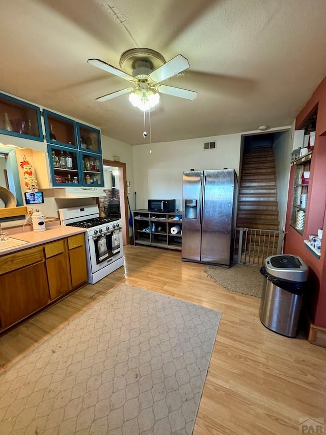 kitchen featuring visible vents, brown cabinetry, stainless steel fridge with ice dispenser, white gas range, and light countertops