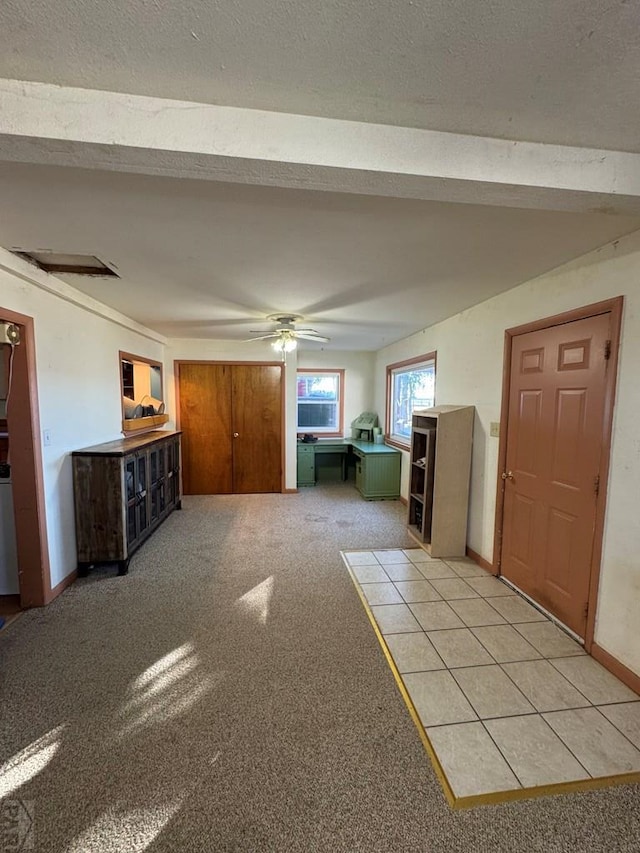 interior space featuring beam ceiling, light colored carpet, ceiling fan, a textured ceiling, and baseboards