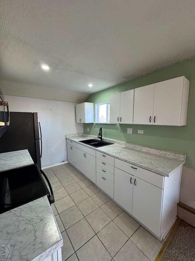 kitchen with white cabinets, freestanding refrigerator, light countertops, a textured ceiling, and a sink