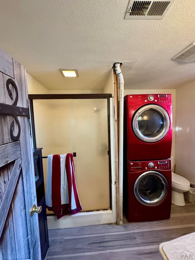 laundry area featuring a textured ceiling, laundry area, wood finished floors, visible vents, and stacked washing maching and dryer