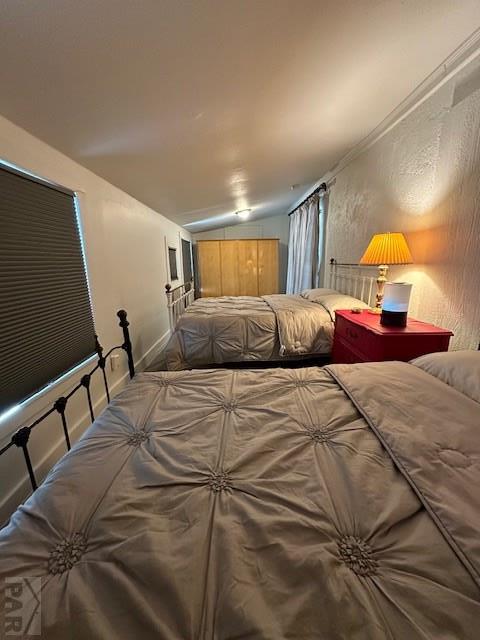 bedroom featuring lofted ceiling, baseboards, and a textured wall