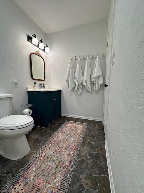 bathroom with baseboards, a textured wall, vanity, and stone tile floors