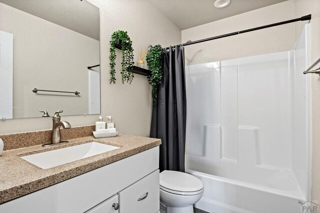 bathroom with a textured wall, shower / tub combo with curtain, vanity, and toilet