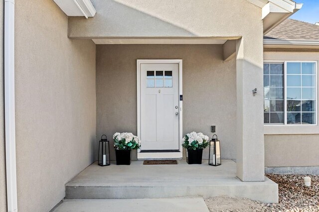 view of exterior entry with a porch, roof with shingles, and stucco siding