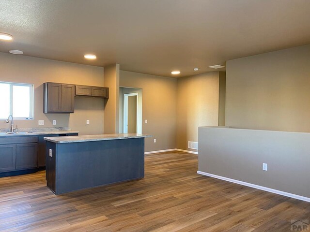 kitchen featuring visible vents, dark wood-style floors, a center island, light countertops, and a sink