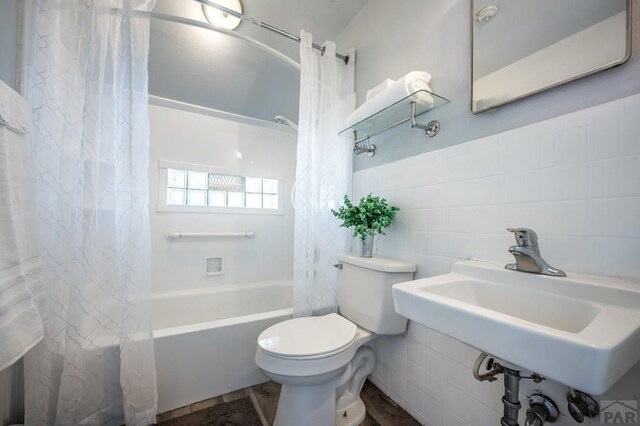 bathroom with a sink, shower / bath combination with curtain, toilet, and tile walls