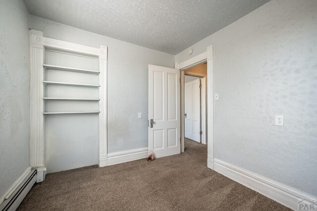 unfurnished bedroom featuring a baseboard heating unit, a textured wall, a textured ceiling, and carpet