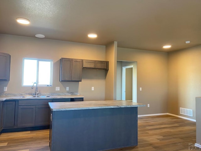 kitchen featuring a center island, visible vents, wood finished floors, and a sink