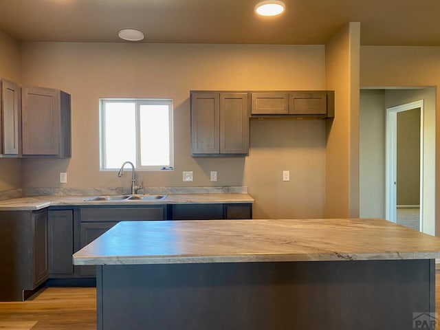 kitchen with a sink, light wood-type flooring, a center island, and light countertops