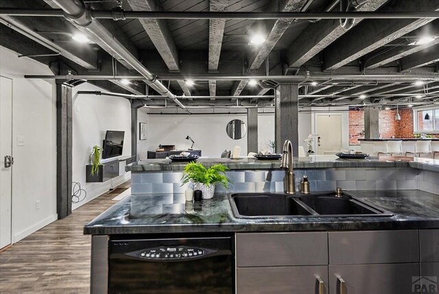 kitchen with dishwasher, dark stone countertops, a sink, and wood finished floors