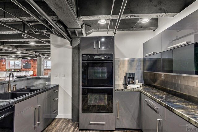 kitchen with dark wood-style floors, a sink, dark stone countertops, modern cabinets, and black appliances