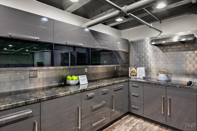 kitchen featuring wall chimney range hood, black electric cooktop, dark stone counters, and light wood-style flooring