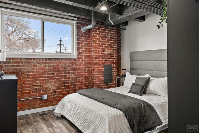 bedroom with brick wall, wood finished floors, visible vents, and baseboards