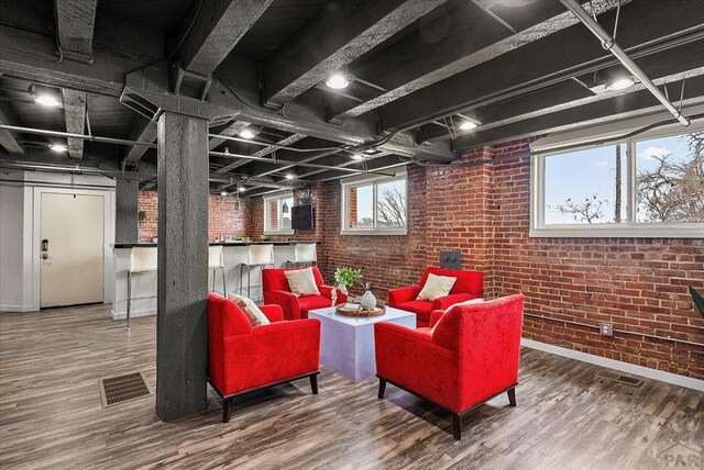 interior space with baseboards, visible vents, brick wall, and wood finished floors